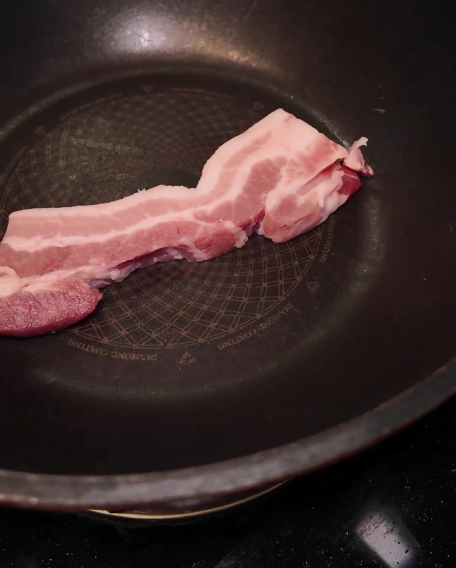 Eine dicke Scheibe roher Schweinebauch in einer großen schwarzen Pfanne.