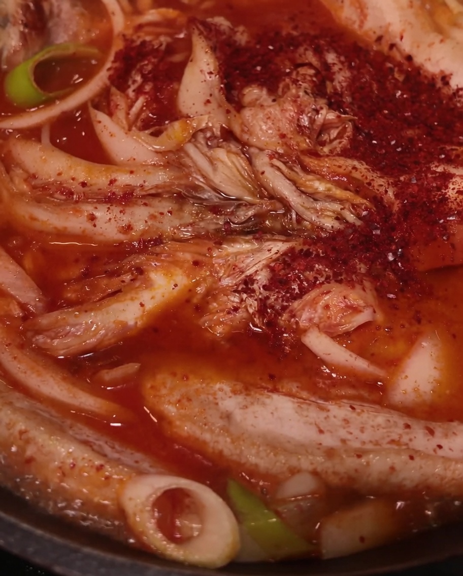 Rotes Chilipulver wird über Schweinefleisch, Kimchi und Zwiebeln in der Pfanne gestreut.