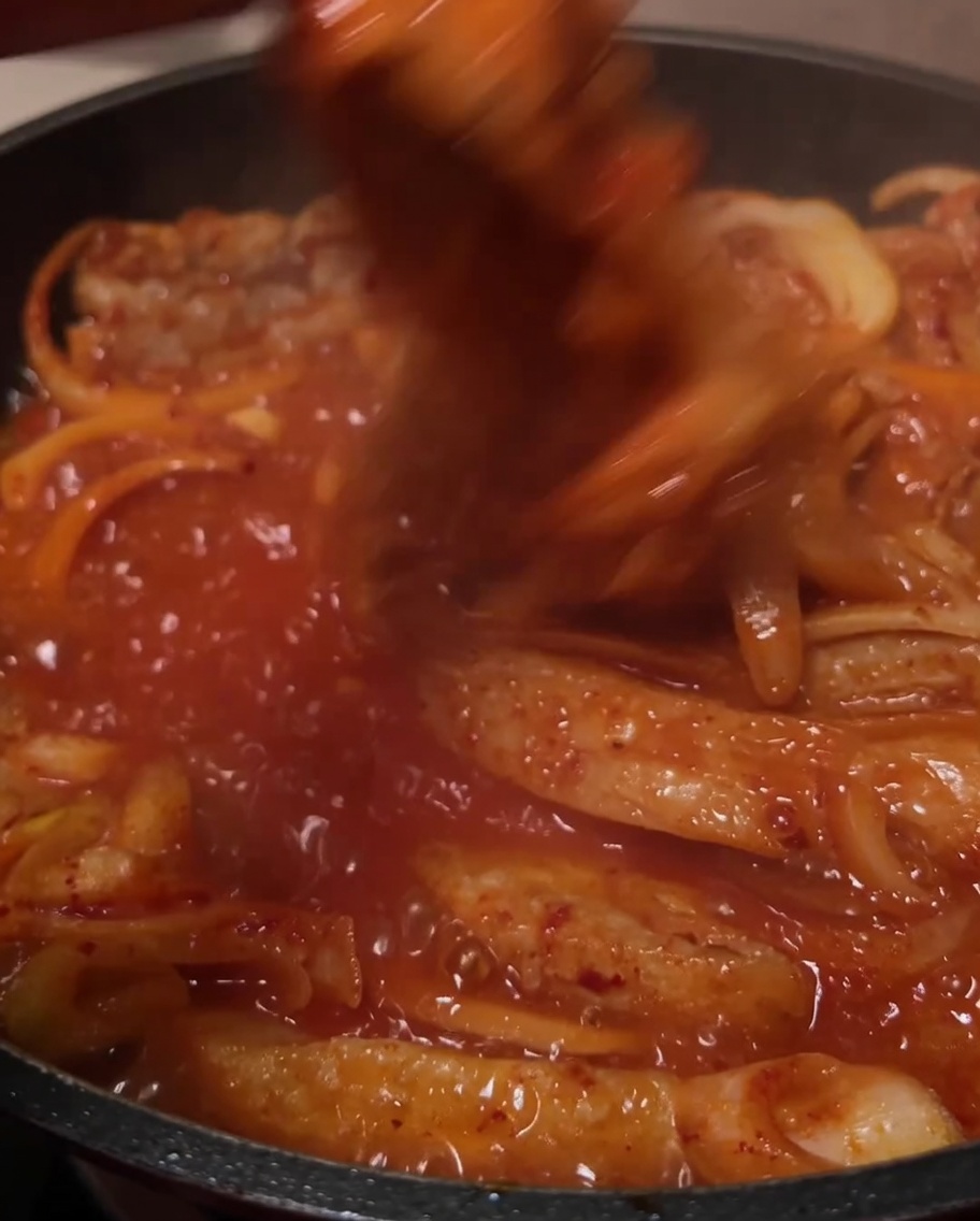 Die Zutaten werden in der sprudelnden roten Sauce in der Pfanne verrührt.