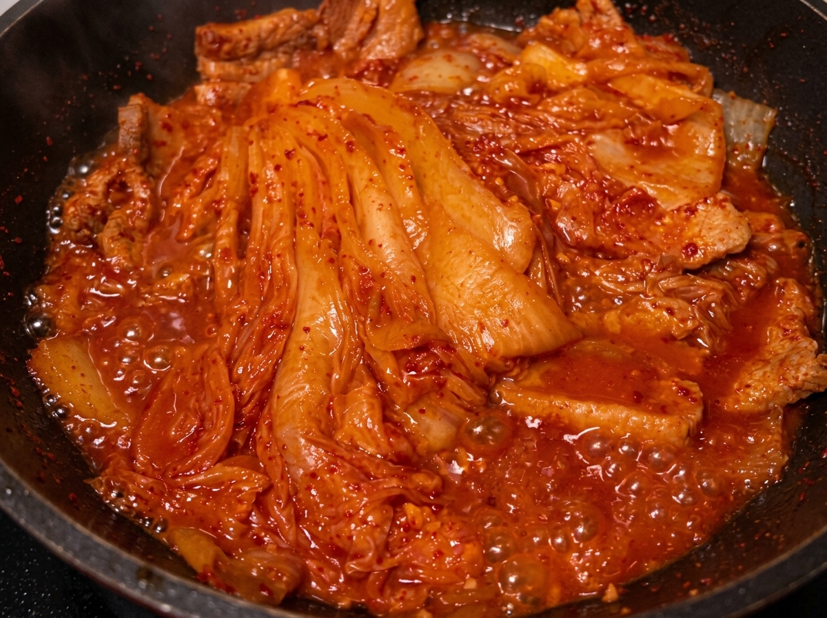 Öl wird von einem Löffel in die Pfanne mit geschmortem Schweinefleisch und Kimchi gegossen.