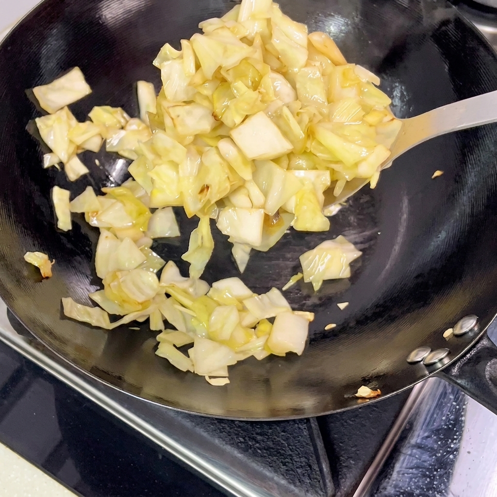 Stücke von eingelegtem Kohl werden mit einem Metallspatel aus dem heißen Wok gehoben.