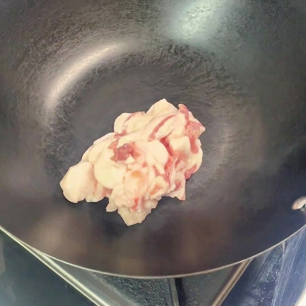 Ein Haufen roher, in Scheiben geschnittener Schweinebauch liegt in der Mitte eines leeren, vorgeheizten Woks.