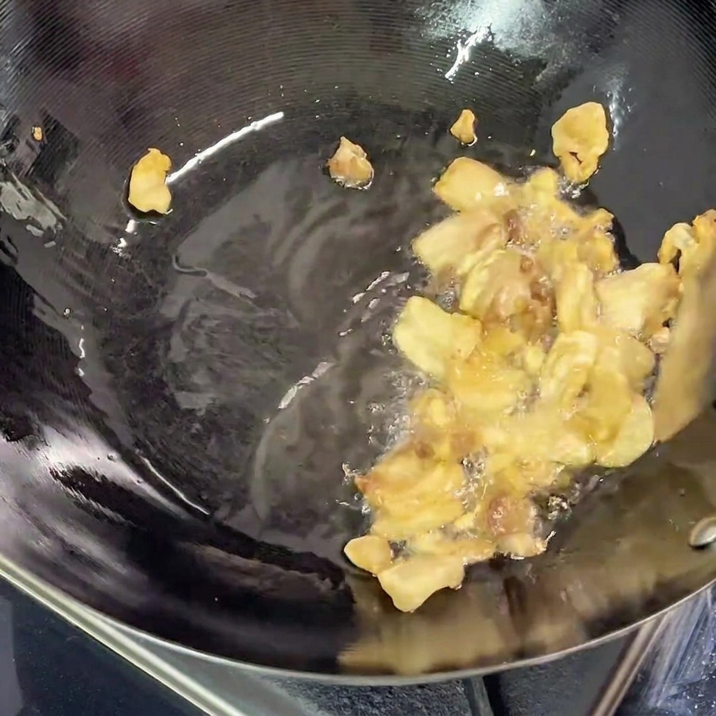 Schweinebauchstücke braten im Wok, auf dem Boden der Pfanne hat sich klares, ausgelassenes Fett gebildet.