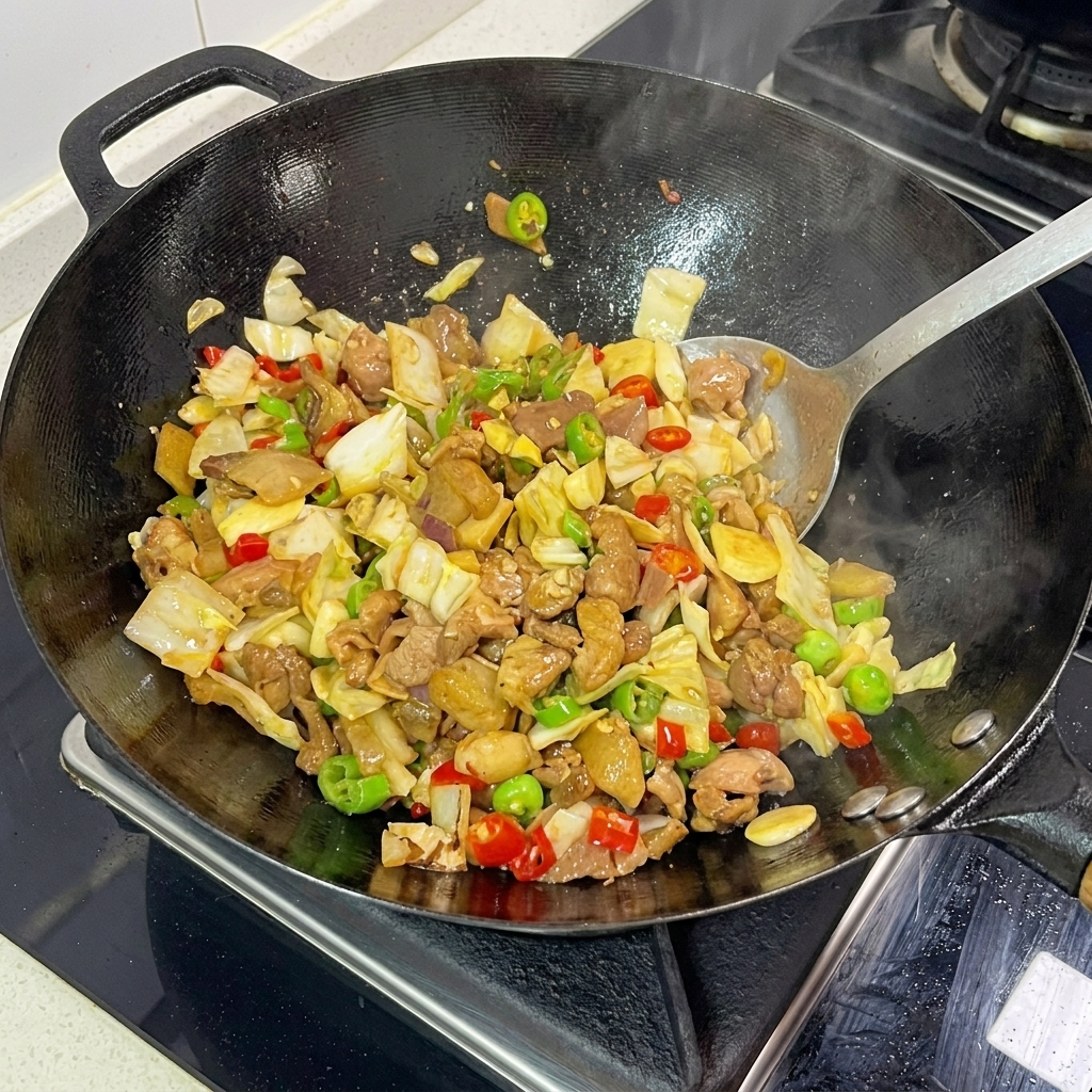 Ein Spatel wendet aktiv eingelegten Kohl, Schweinefleisch und gehackte Chilis in einem dampfend heißen Wok.