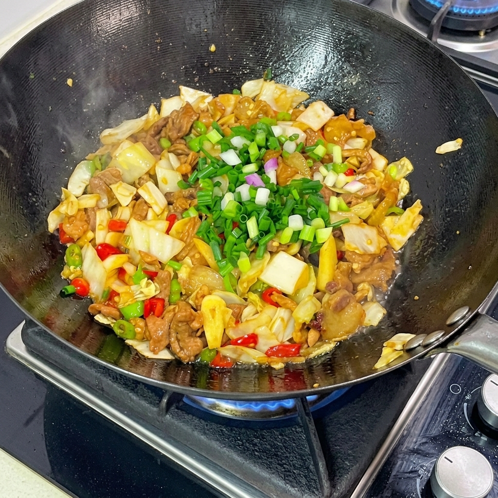 Leuchtend grüne, gehackte Frühlingszwiebeln werden großzügig über den fertigen Wok-Kohl mit Schweinefleisch gestreut.
