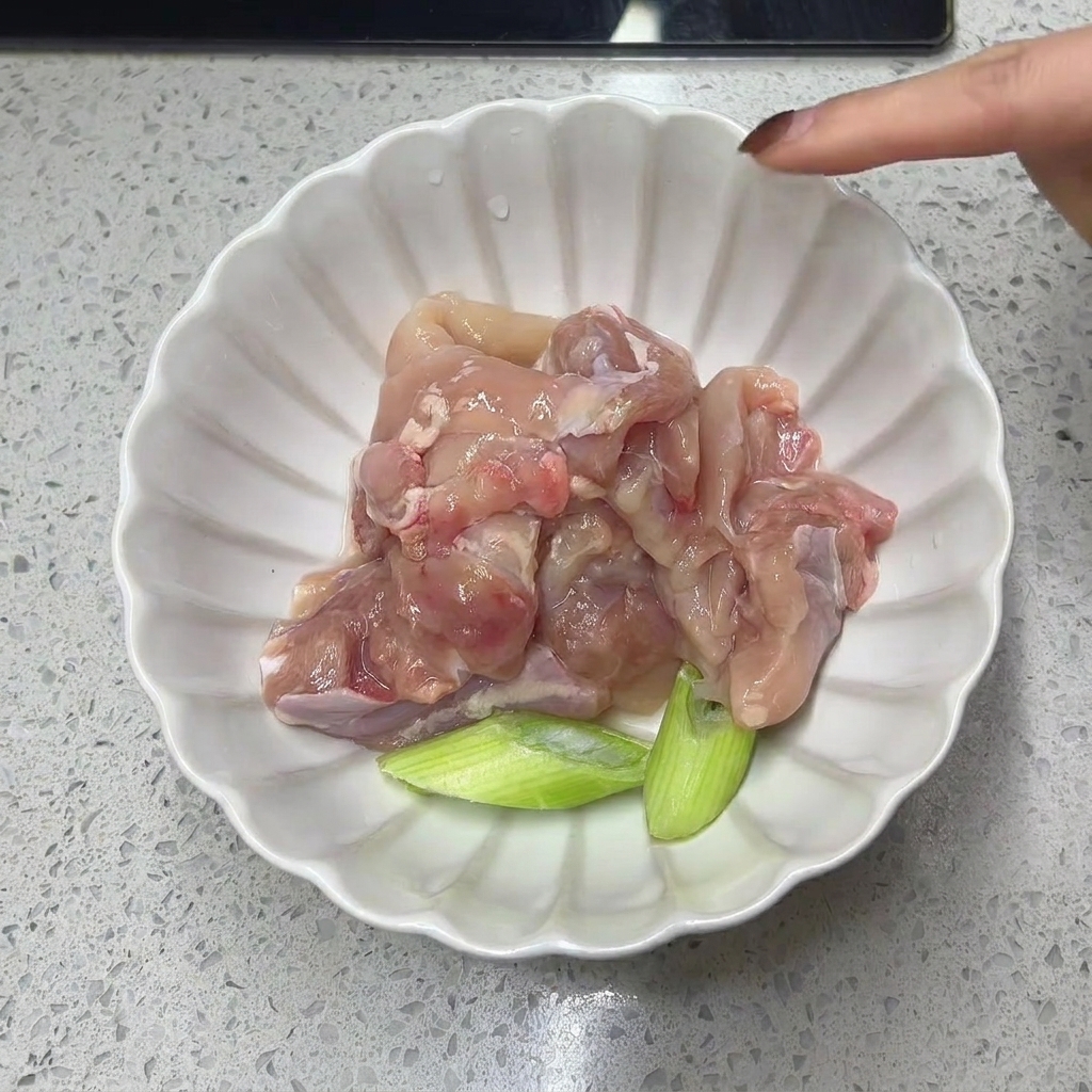 Rohes, entbeintes Hähnchenschenkelfleisch und Frühlingszwiebelstücke in einer weißen Schale.