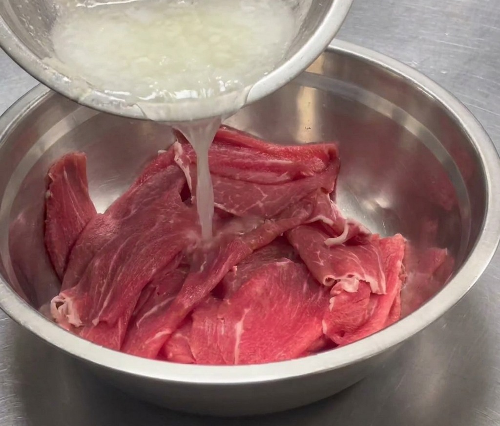 Aromatisches Püree wird über das geschnittene Rindfleisch in einer Edelstahlschüssel gegossen.