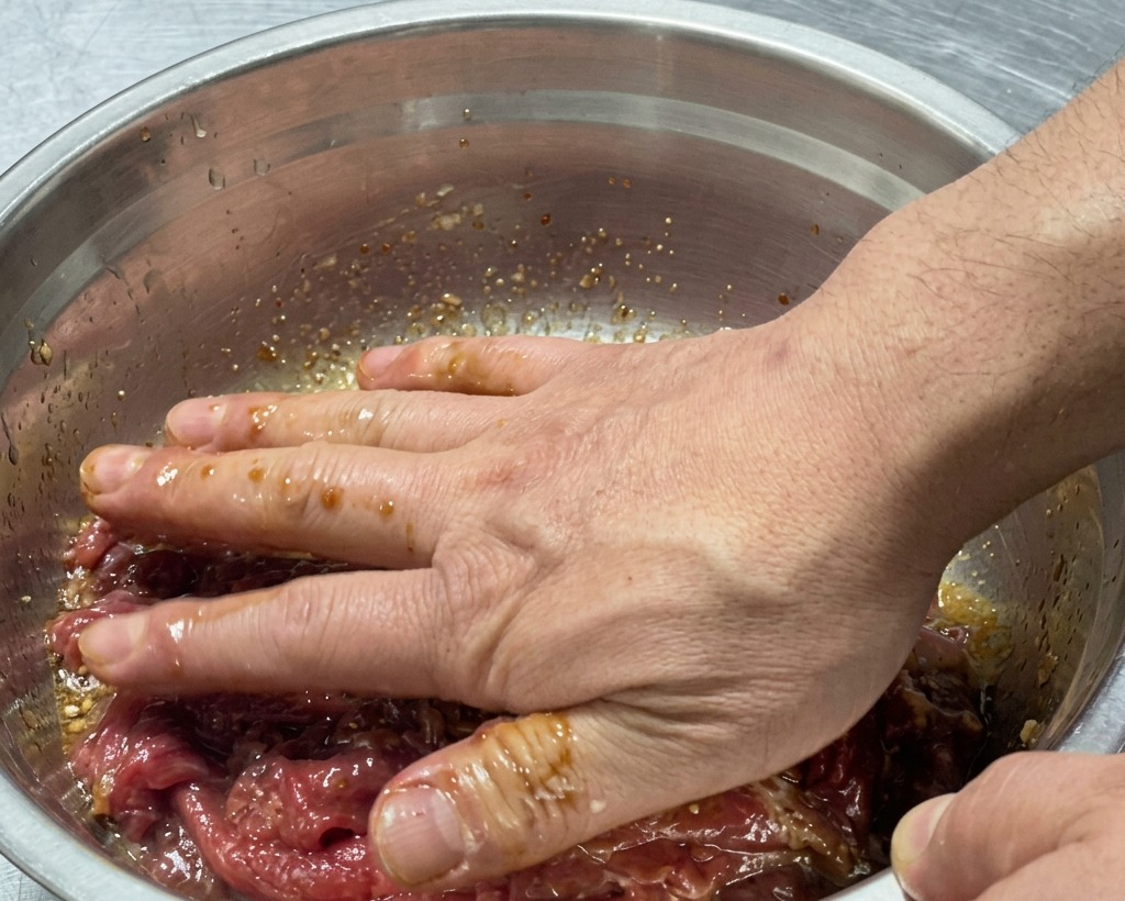 Hände vermengen das rohe Fleisch mit der Marinade in der Schüssel.