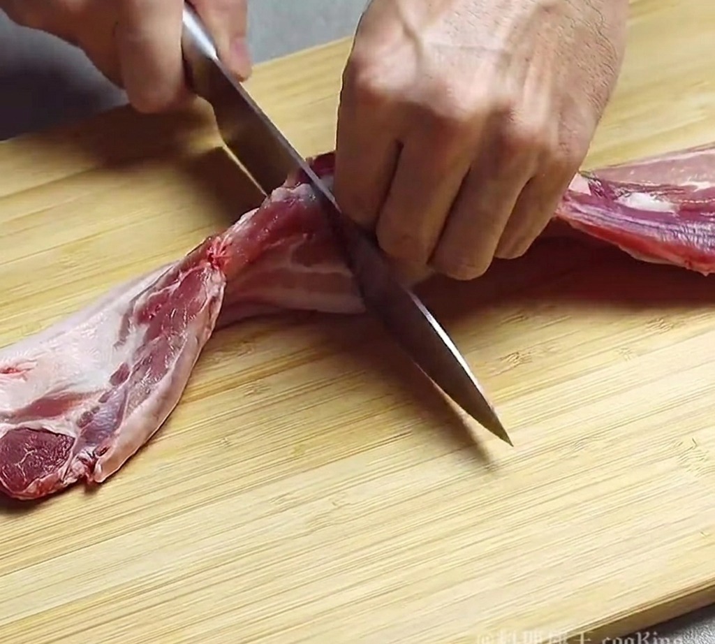 Eine Person benutzt ein Kochmesser, um rohen Schweinebauch auf einem Holzbrett in dicke Streifen zu schneiden.