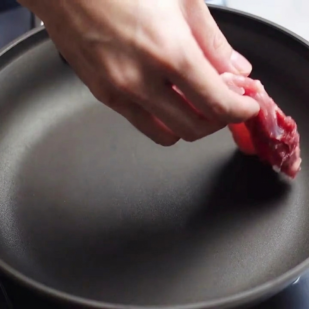 Rohe, gewürzte Schweinebauchstreifen werden in eine vorgeheizte Pfanne gelegt.