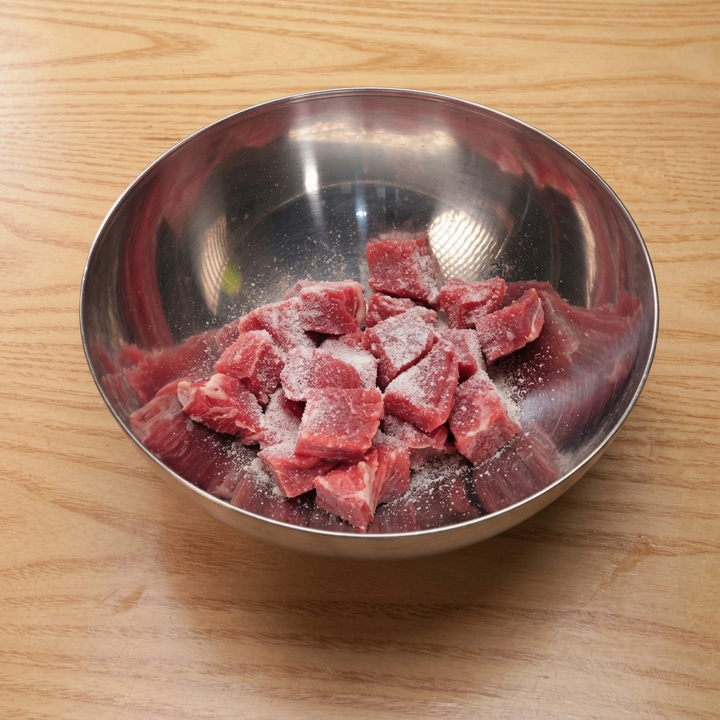 Rinderwürfel in einer Metallschüssel werden mit Salz, Zucker, Sojasauce und Stärke vermengt.