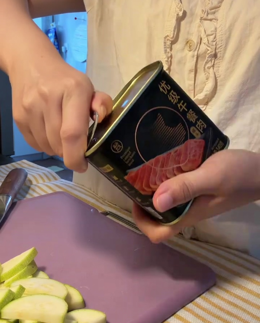 Ein Block Frühstücksfleisch wird aus einer geöffneten Metalldose genommen.
