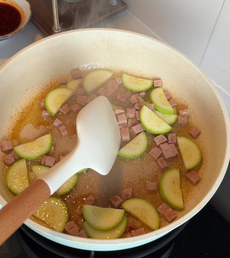 Zucchinischeiben und gewürfeltes Frühstücksfleisch braten zusammen in einer Antihaftpfanne.