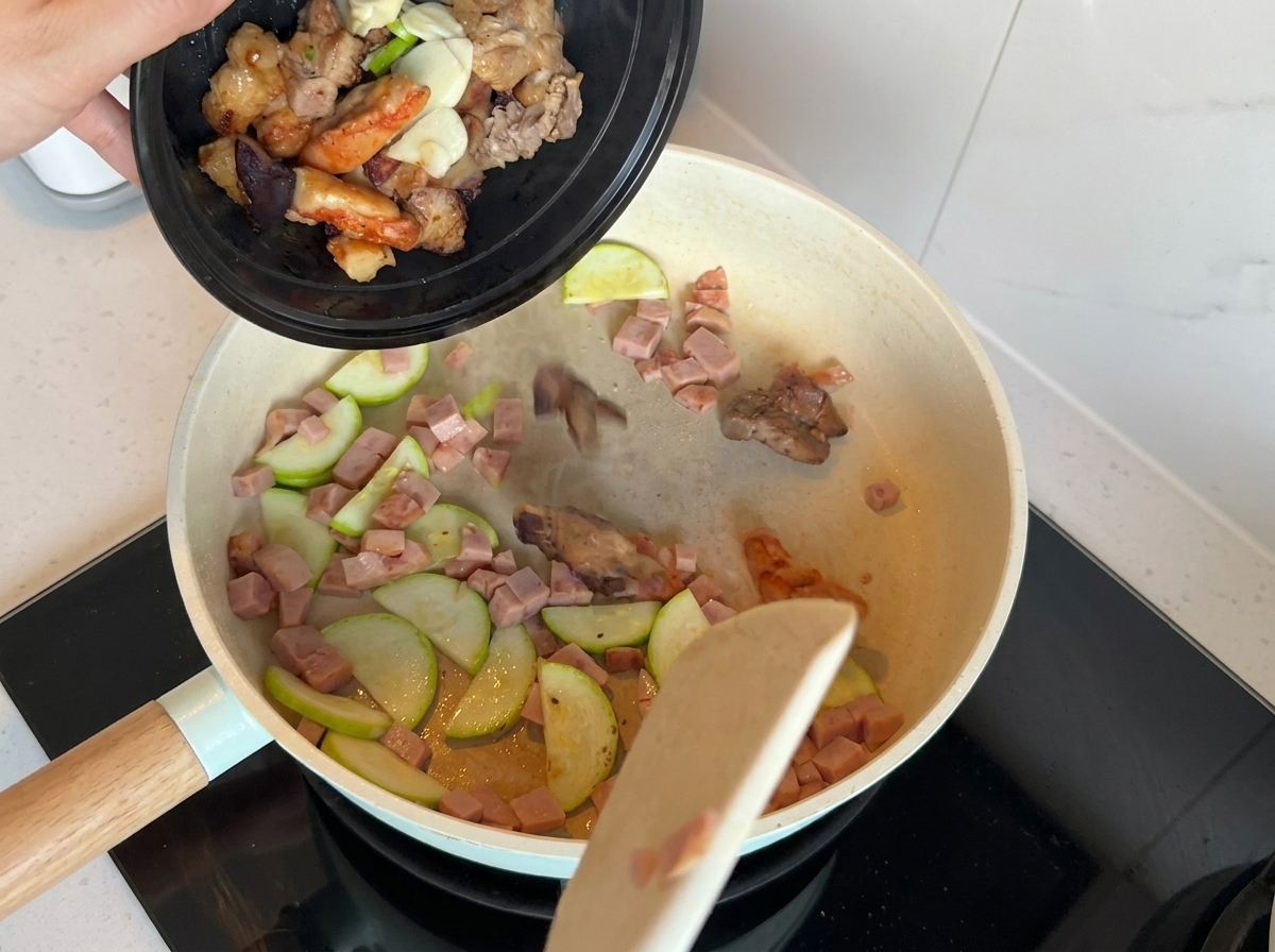 Eine Pfanne mit gebratener Zucchini und Frühstücksfleisch, angereichert mit Frühlingszwiebeln, Knoblauch und weiteren Fleischstücken.