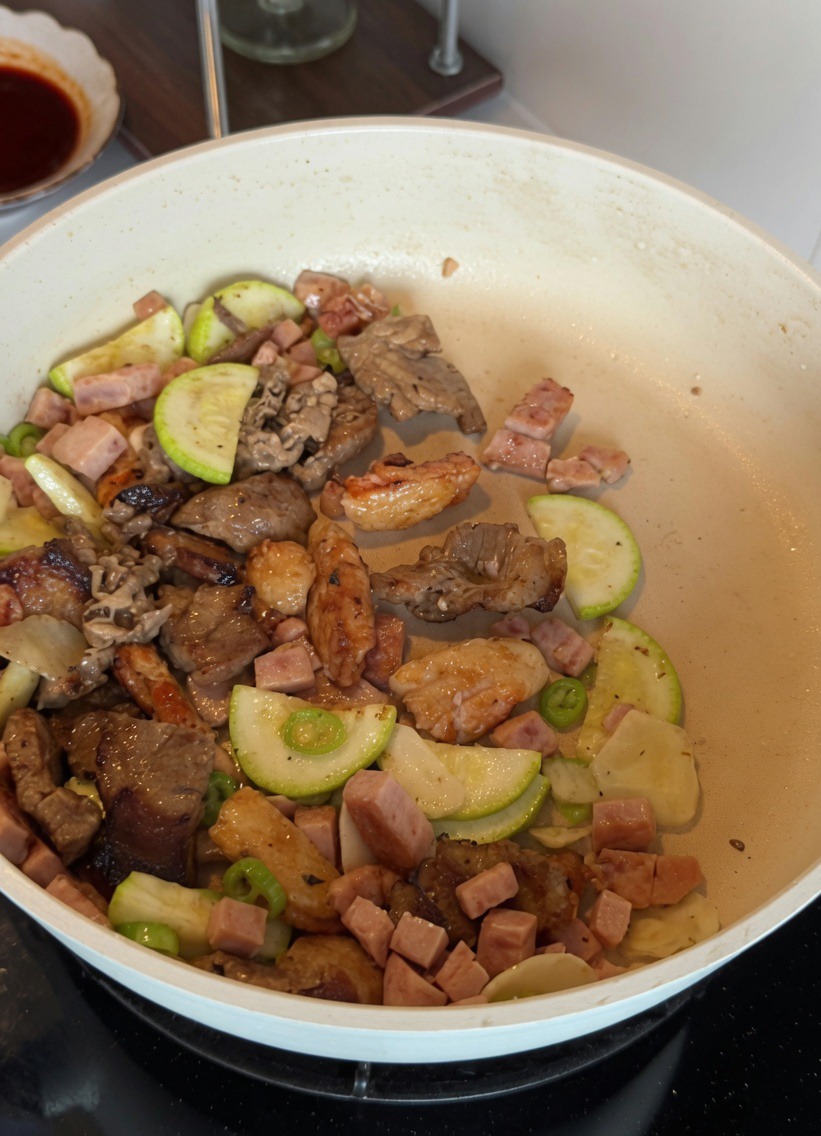 Die verquirlte Eiermischung wird zusammen mit Zucchini und Fleisch in einer weißen Pfanne verrührt.