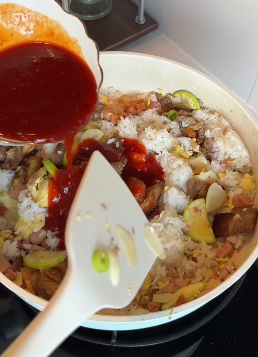 Koreanische Bibimbap-Sauce wird über den Reis und die Zutaten in der Pfanne gegossen.