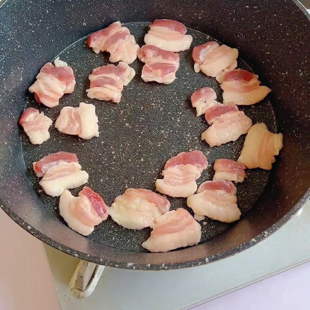 Rohe Schweinebauchscheiben in einer heißen Pfanne, die langsam bräunen.