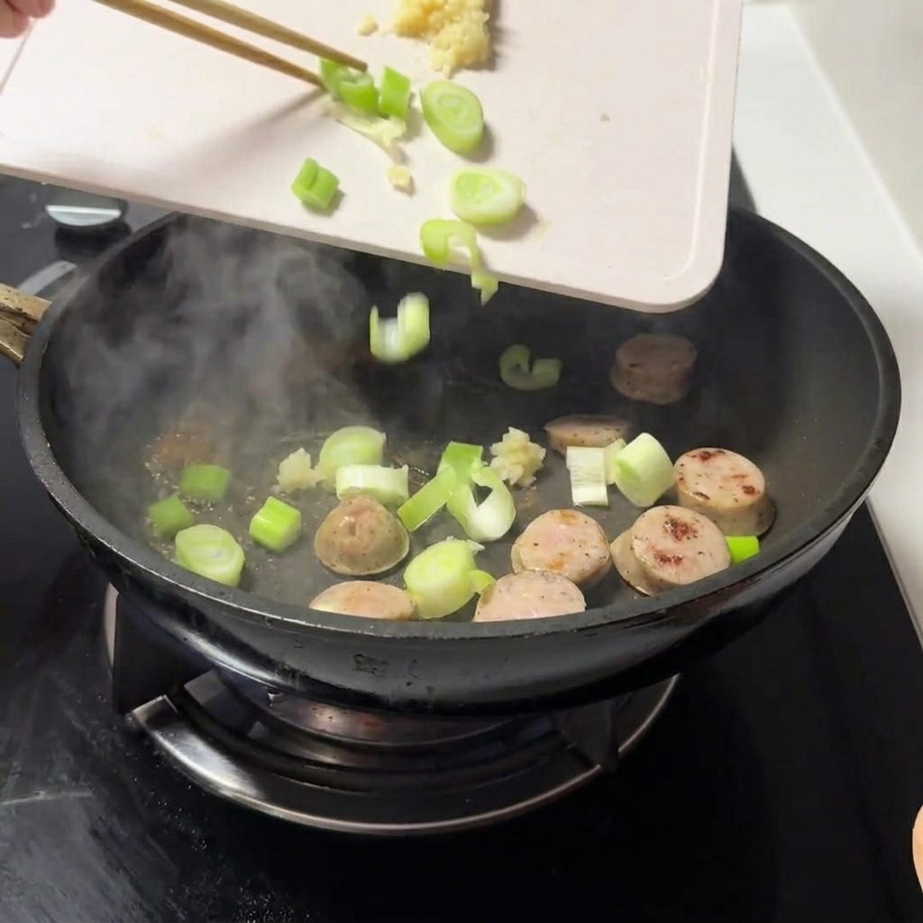 Frisch gehackte Frühlingszwiebeln und fein gehackter Knoblauch werden zu dem Fleisch in die Pfanne gegeben.