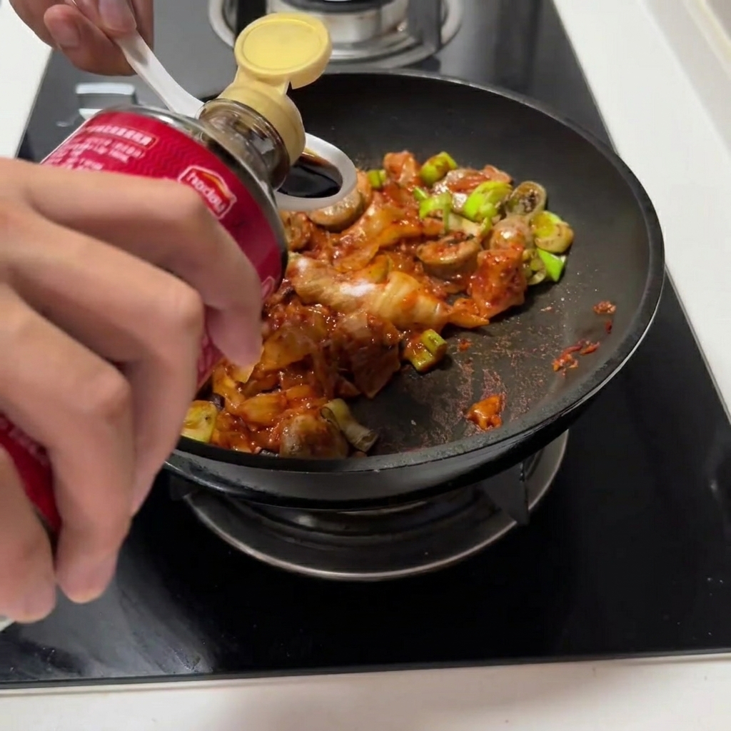 Sojasauce und Austernsauce werden zur Kimchi-Mischung in die Pfanne gegossen.
