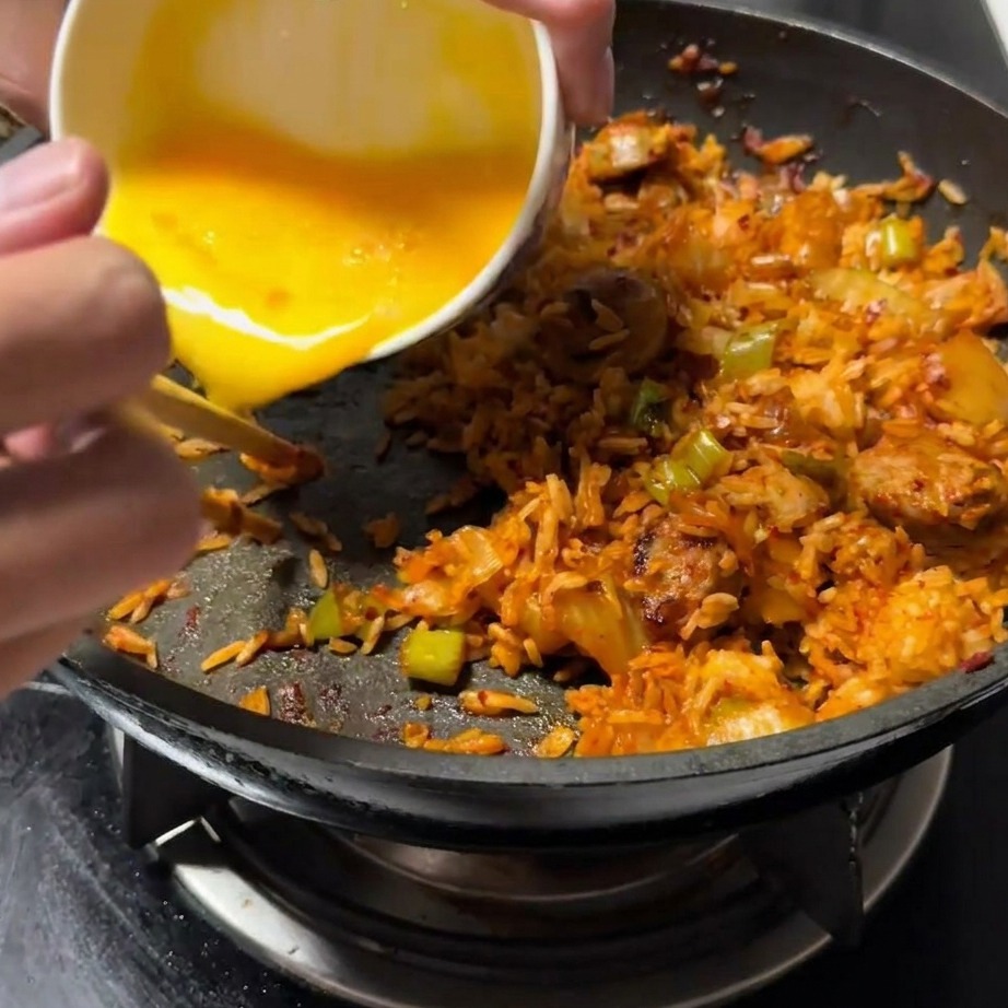 Verquirltes Ei wird auf eine freigeräumte Seite der Pfanne neben der Bratreismischung gegossen.