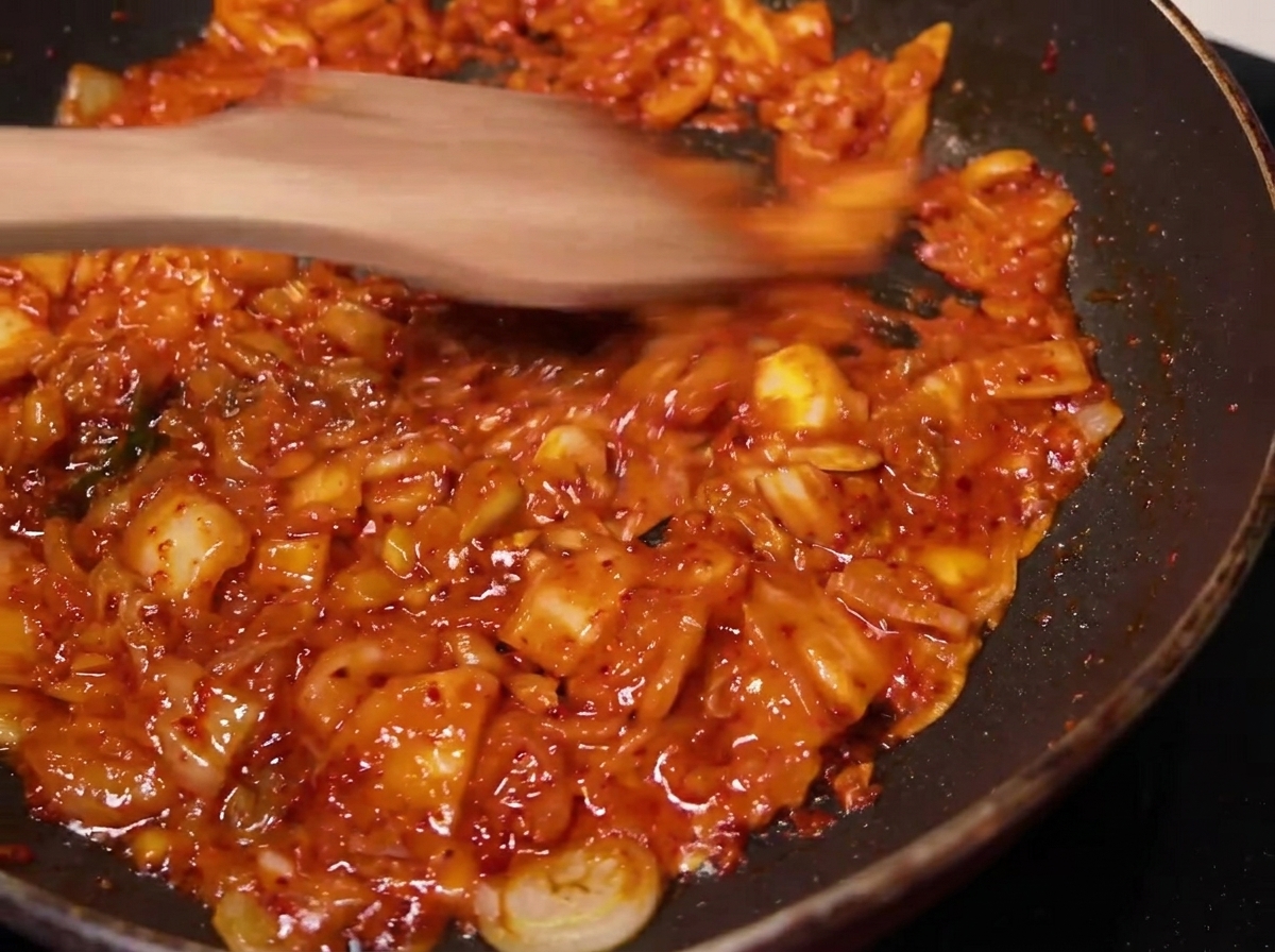 Die gewürzte Kimchi-Mischung wird in einer Pfanne mit einem Holzspatel gerührt und gebraten.