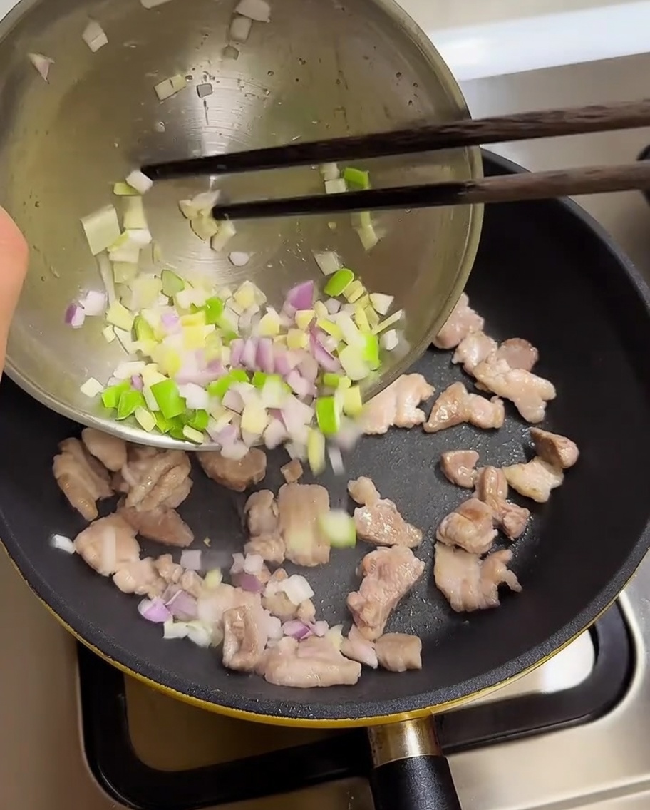 Gehackte Frühlingszwiebeln, Knoblauch und Zwiebeln werden in eine Pfanne mit gebratenem Schweinebauch gegeben.