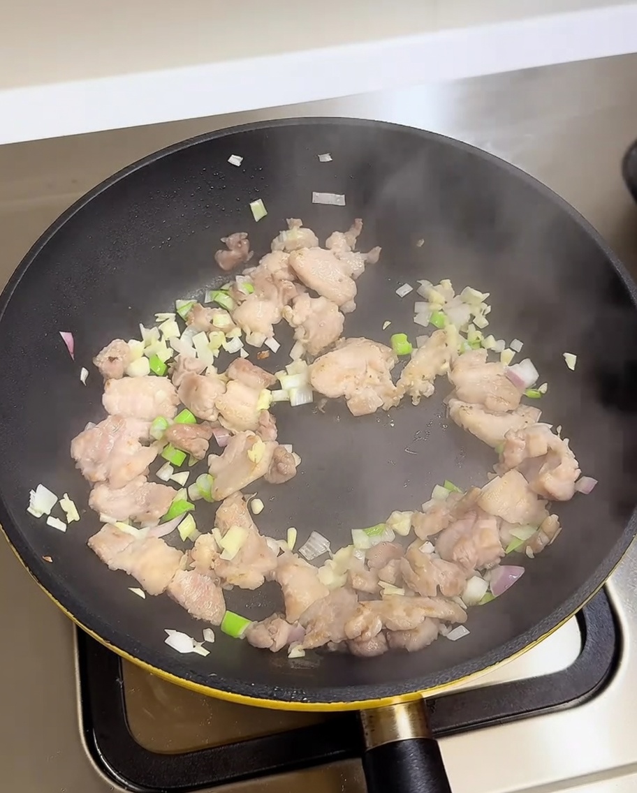 Schweinebauch, Frühlingszwiebeln, Knoblauch und Zwiebeln werden in einer Pfanne mit Würzflüssigkeiten angebraten.