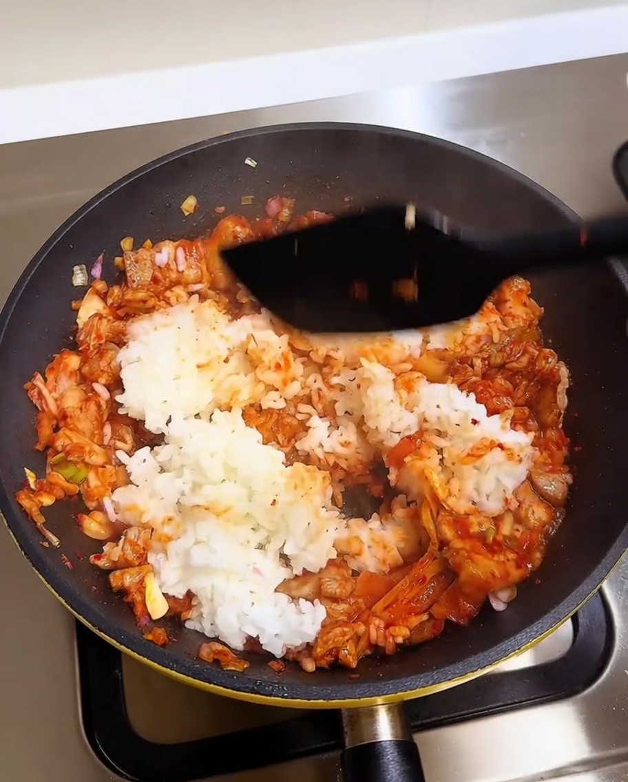 Ein Pfannenwender mischt weißen Reis in eine lebendig rote Fleisch-Kimchi-Basis in einer heißen Pfanne.
