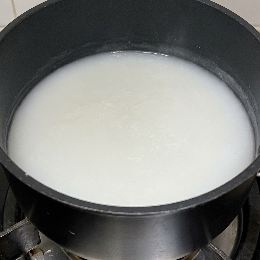 Eine dicke, weiße Klebreismehl-Paste kocht in einem schwarzen Topf.