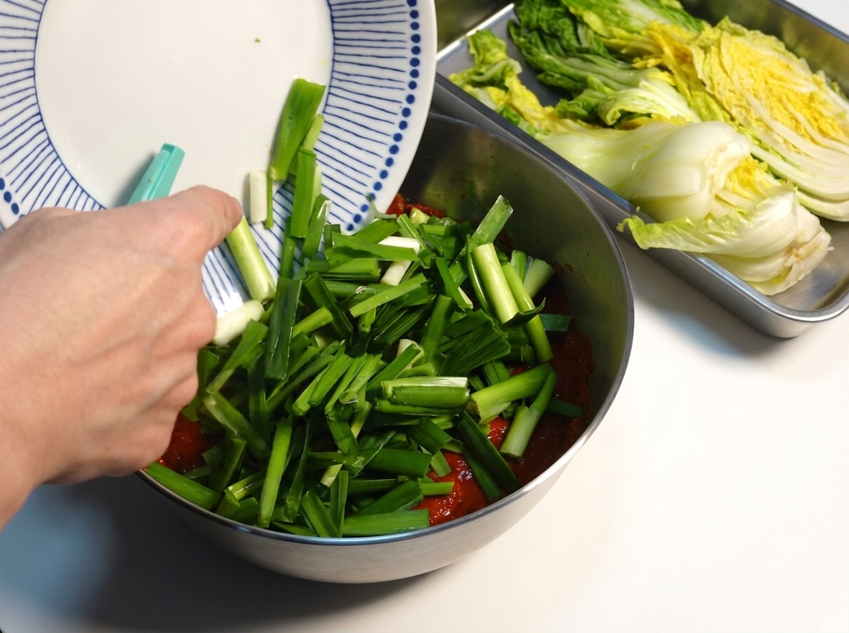 Frisch gehackter Schnittlauch wird in einer Metallschüssel zu einer dicken roten Kimchi-Gewürzpaste hinzugefügt.