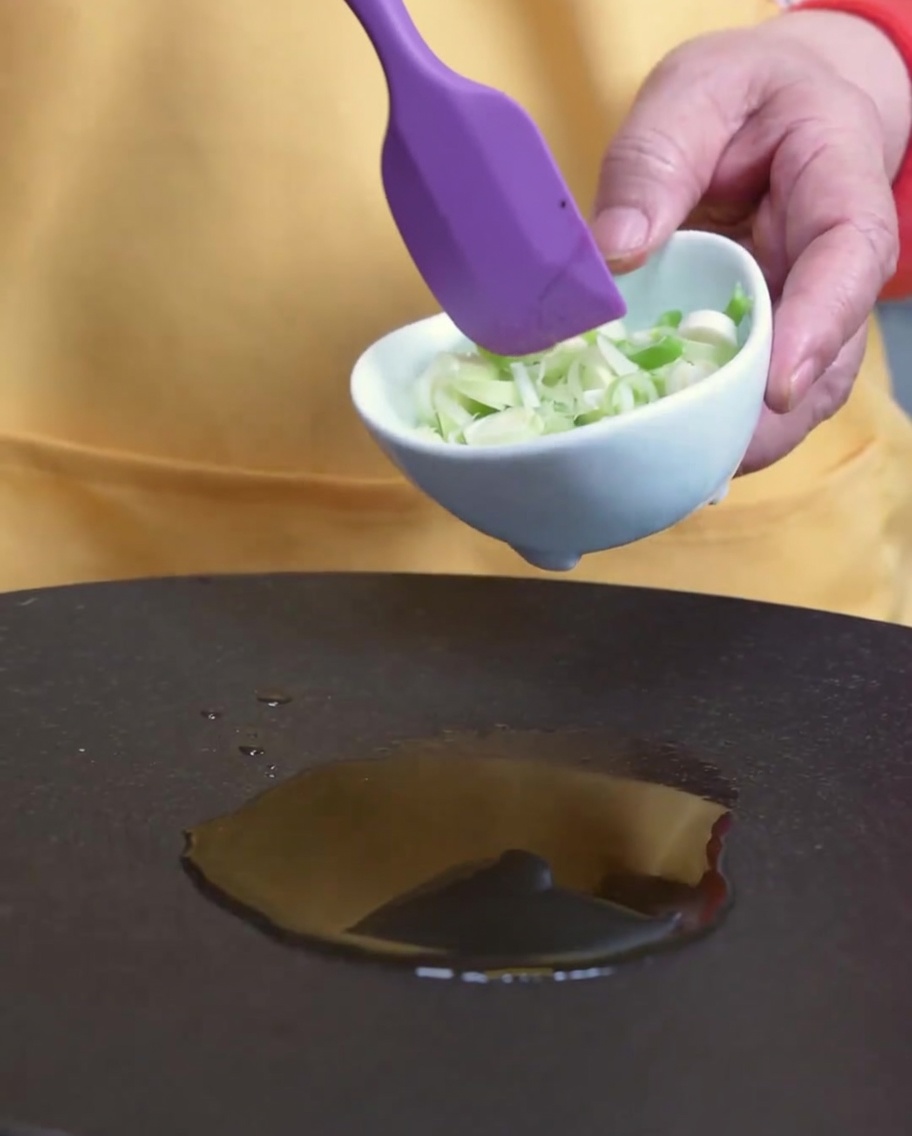 Frühlingszwiebeln werden in einer Pfanne mit Sesamöl angebraten.
