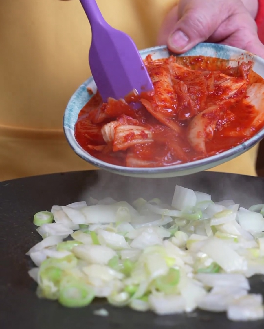 Kimchi wird zu den bereits in der Pfanne garenden Frühlingszwiebeln gegeben.