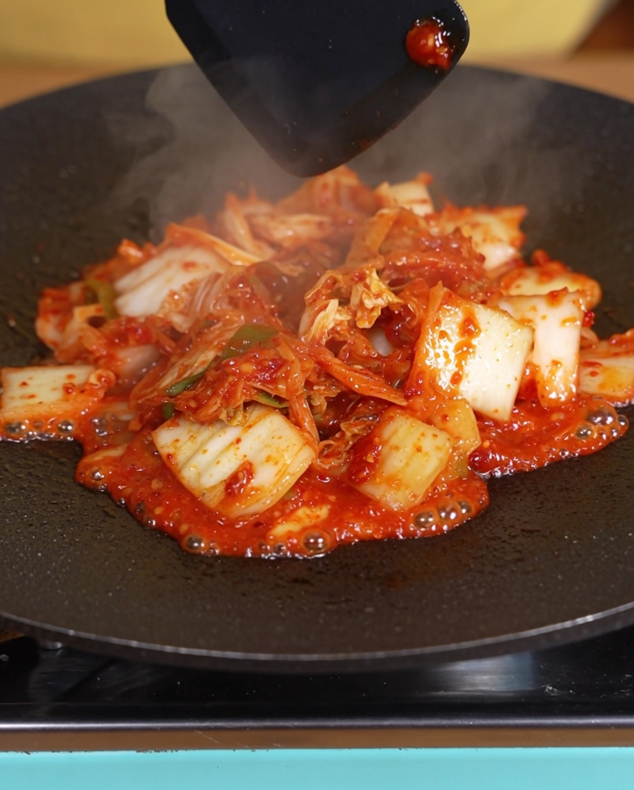 Kimchi wird in der Pfanne gebraten, wobei die Flüssigkeit bereits sichtlich reduziert ist.