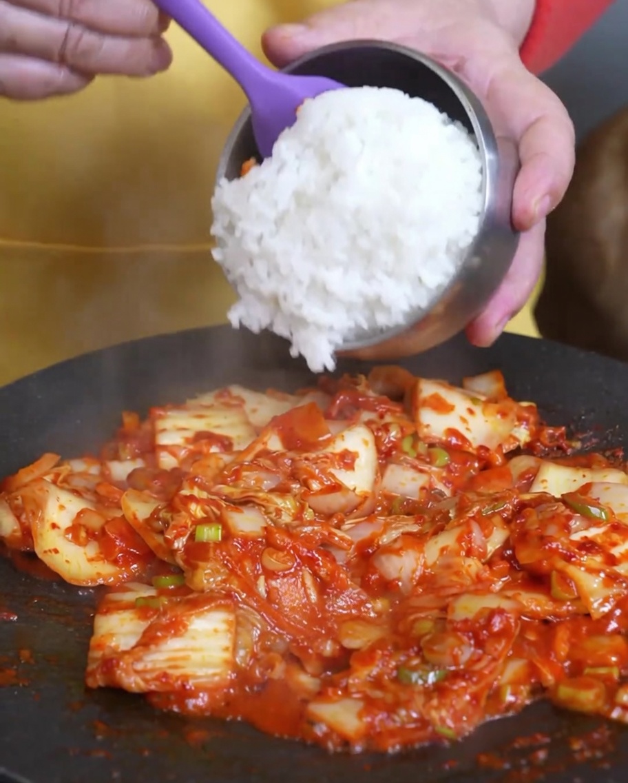 Gekochter weißer Reis wird in die Pfanne zu dem gebratenen Kimchi gegeben.