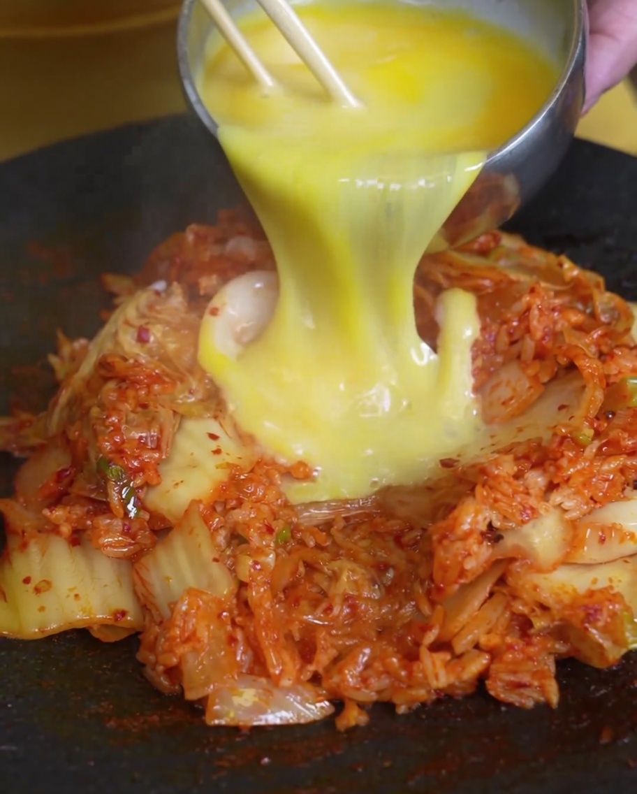 Verquirlte Eier werden über einen Berg Kimchi-Reis in einer heißen Pfanne gegossen.