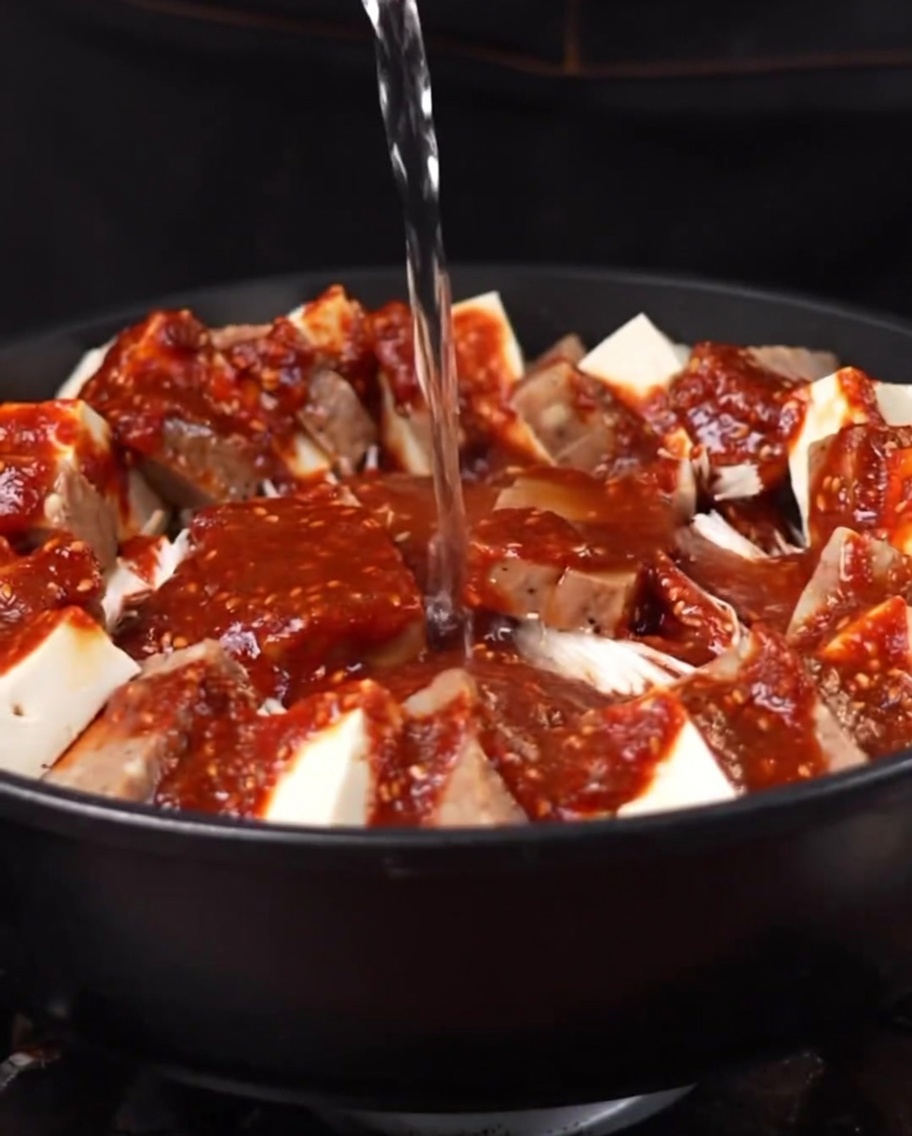Kochendes Wasser wird in den Topf gegossen und beginnt sich mit der Sauce und den Zutaten zu vermischen.
