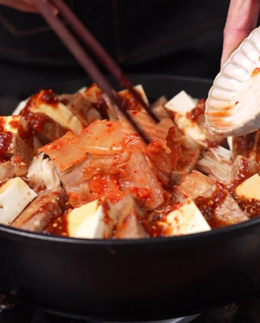 Ein Häufchen Kimchi wird in die Mitte des Topfes gegeben, umgeben von den anderen Zutaten.