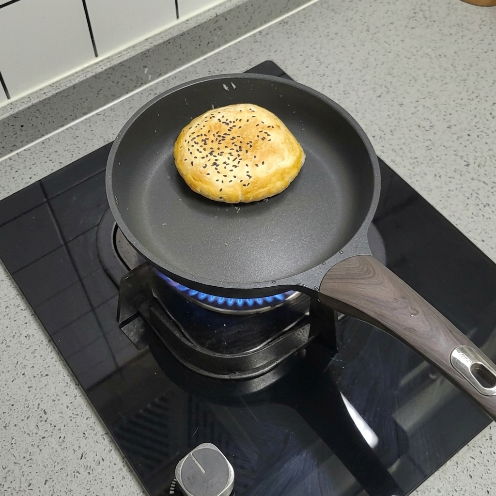 Ein gefrorenes Burgerbrötchen mit Sesam in einer trockenen Pfanne auf dem Herd.