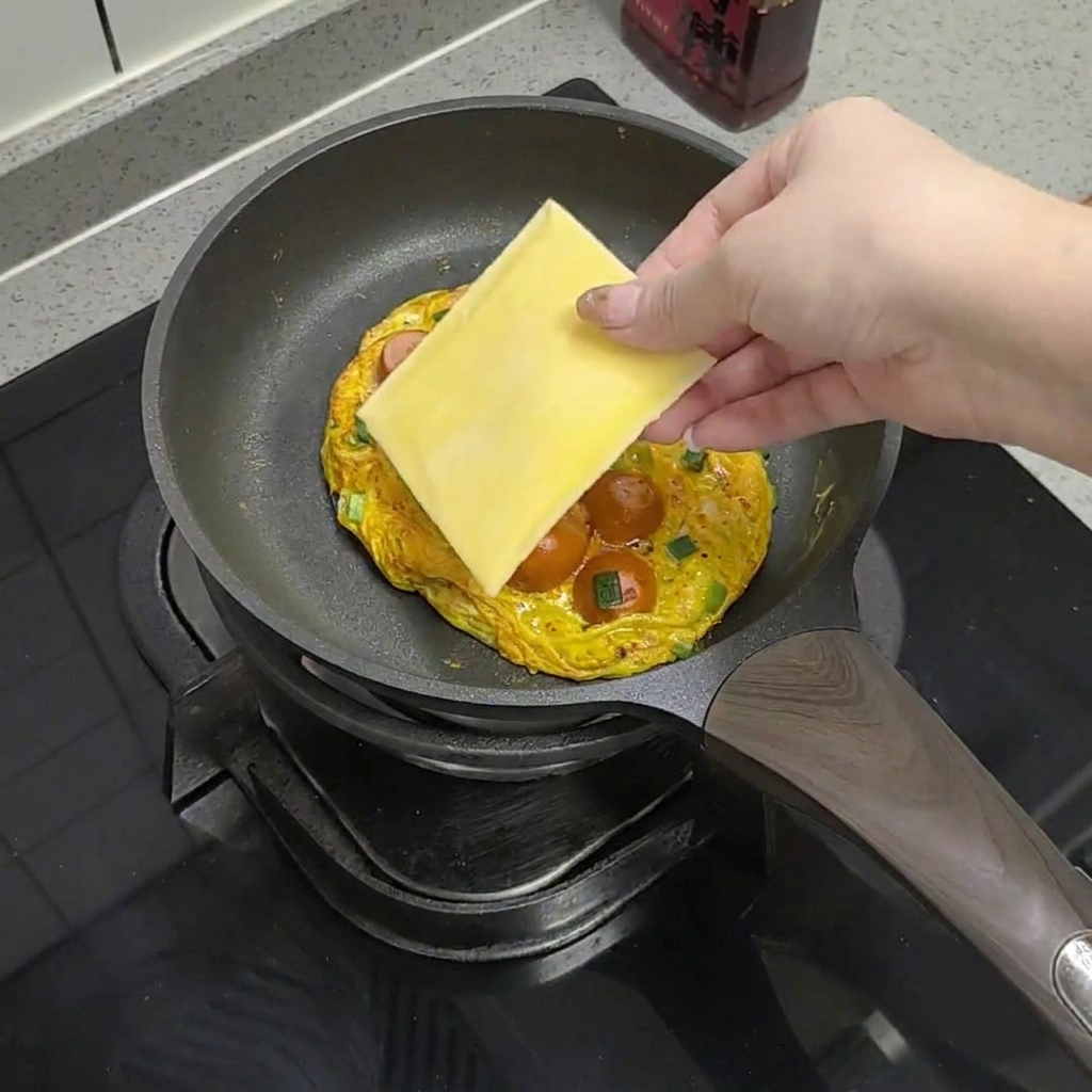 Eine Scheibe Käse wird auf die Eimasse in der Pfanne gelegt.