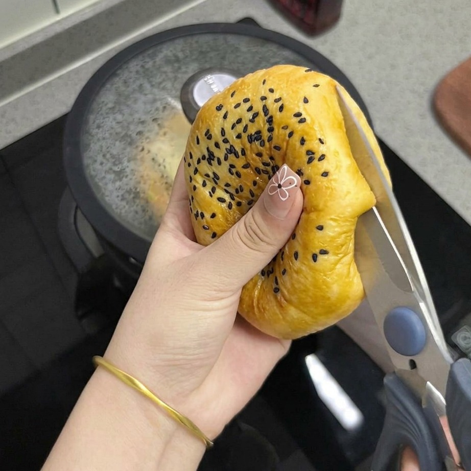 Ein geröstetes Sesambrötchen wird mit einer Küchenschere halbiert.