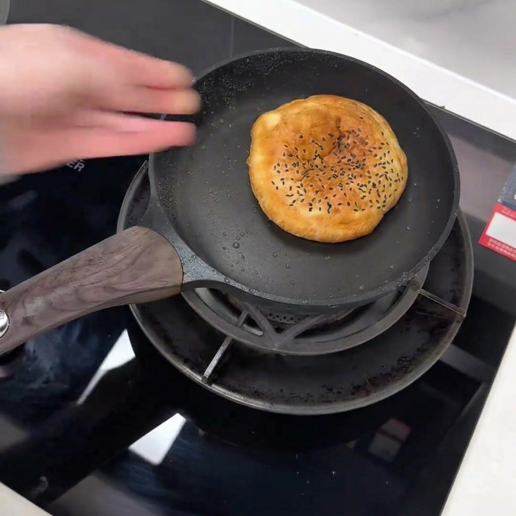 Ein Burger-Bun mit schwarzem Sesam wird in eine beschichtete Pfanne gelegt.