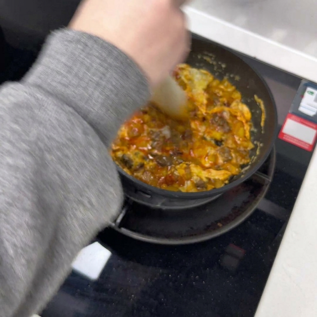 Ein Spatel teilt das stockende Omelett in der Pfanne in zwei Hälften.