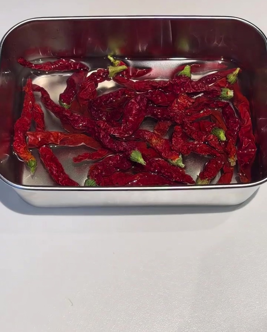 Getrocknete rote Chili-Häute in einem Edelstahlbehälter in heißem Wasser eingeweicht.