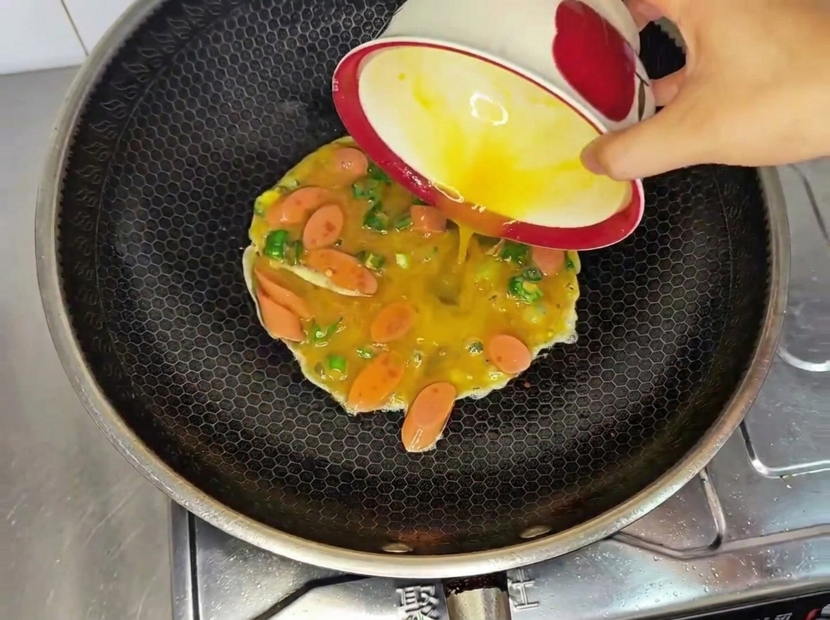 Die Ei-Wurst-Chili-Mischung wird in den heißen Wok gegossen.