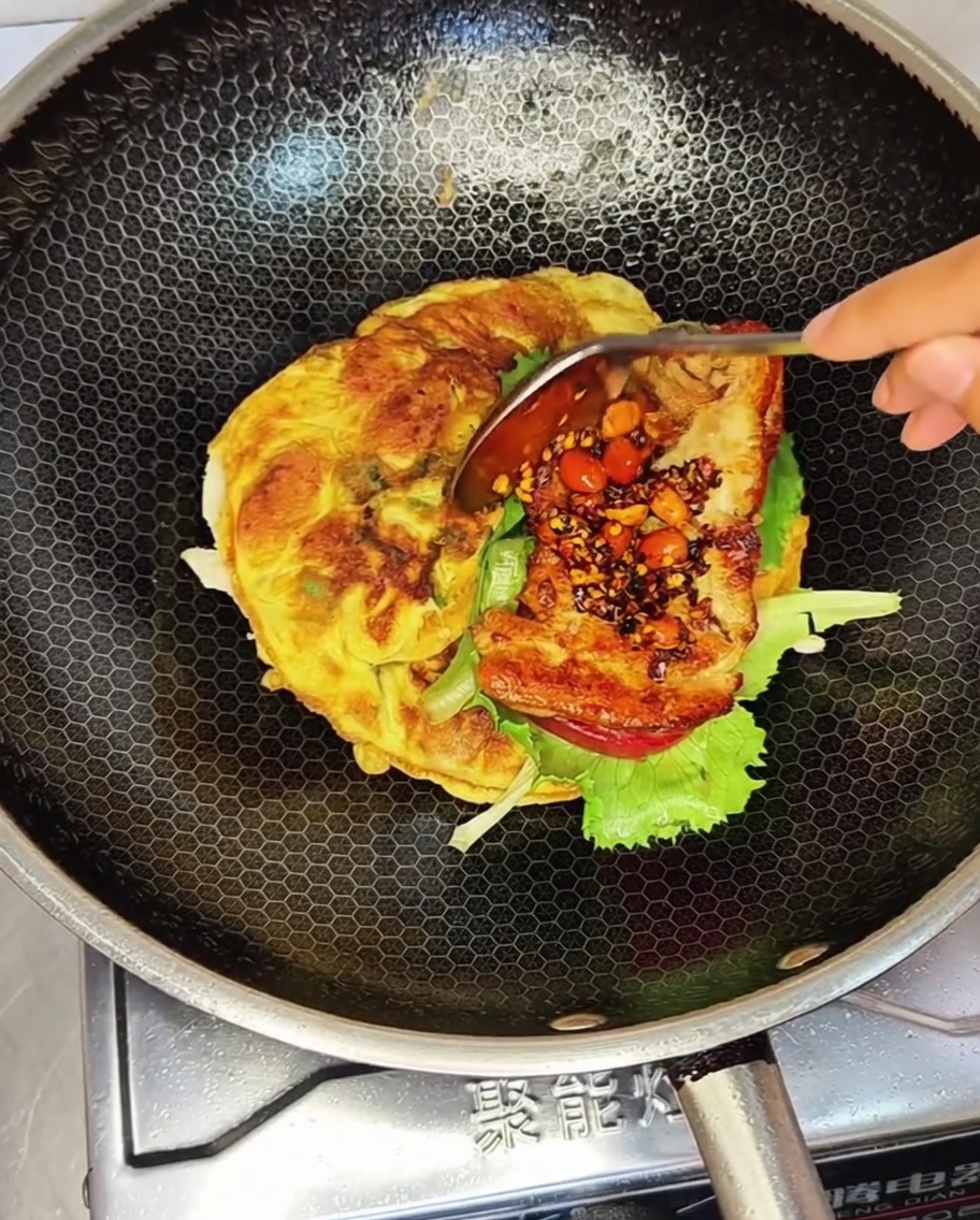 Das Hähnchenpatty mit einer Portion Sauce liegt auf dem Salat im Wok.