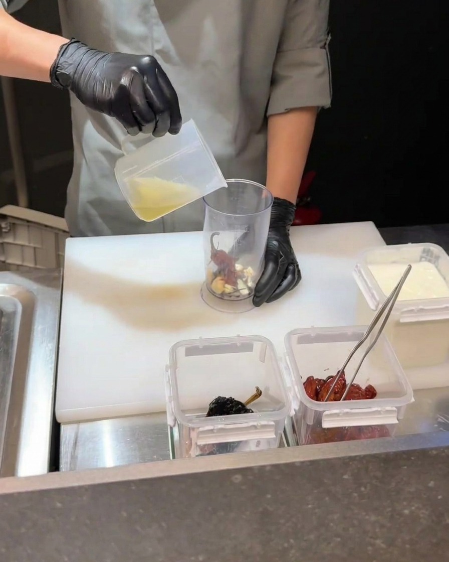 Ein Pürierstab verarbeitet Chilis, Eigelb und Flüssigkeit in einem Behälter.