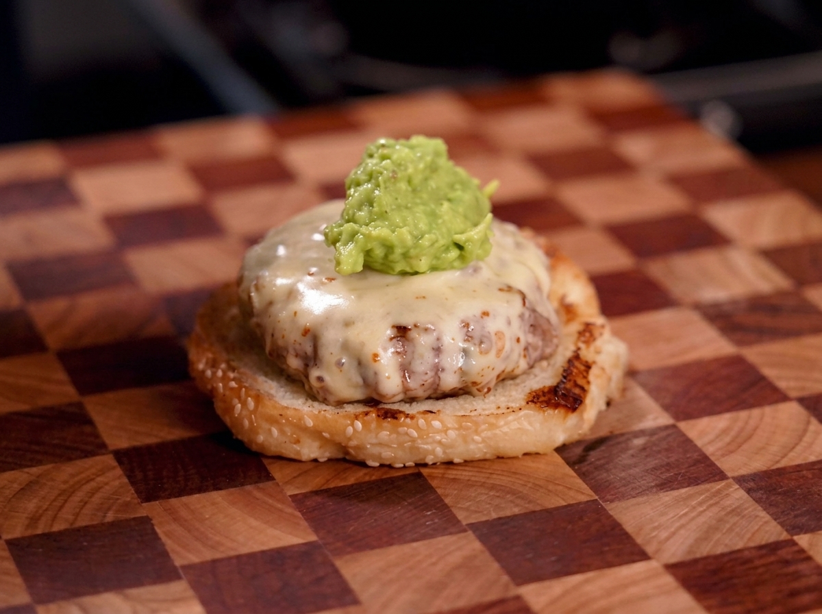 Ein Klecks grobe grüne Guacamole liegt auf einem Käse-Burger-Patty.