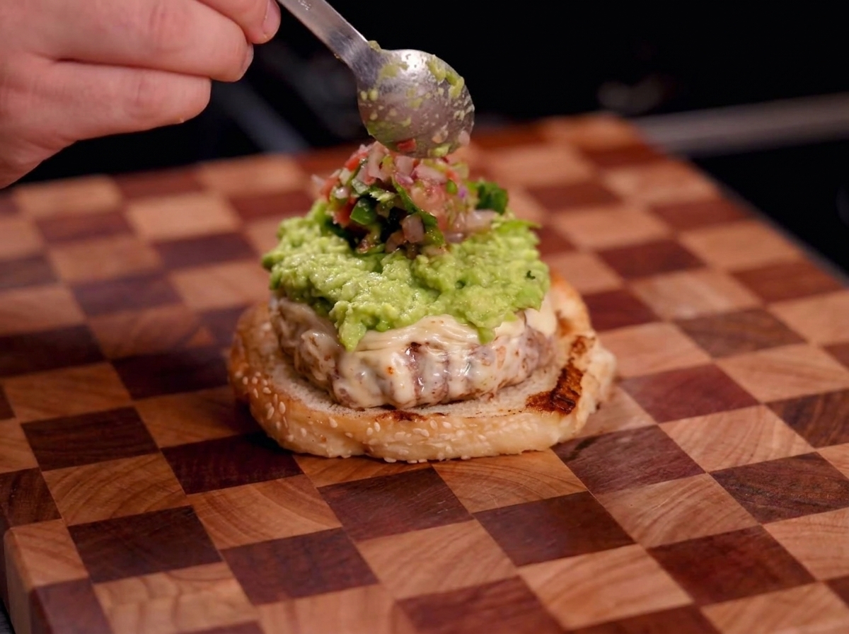 Jemand gibt mit einem Löffel frische rote Salsa auf die Guacamole-Schicht.