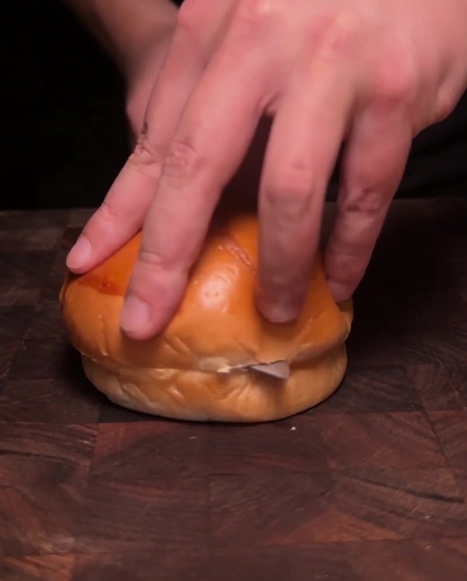 Zwei Burger-Bun-Hälften liegen mit der Schnittfläche nach unten in einer Pfanne und rösten in zerlassener Butter goldbraun.