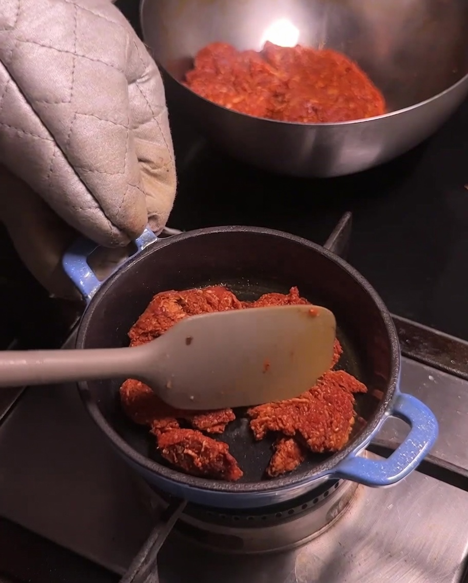Ein kleiner blauer Topf auf dem Herd, in dem zerkleinertes Chorizo-Fleisch mit einem hellen Spatel umgerührt wird.